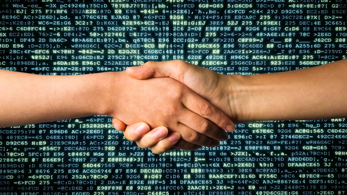 Two people shake hands. In the background is computer code.