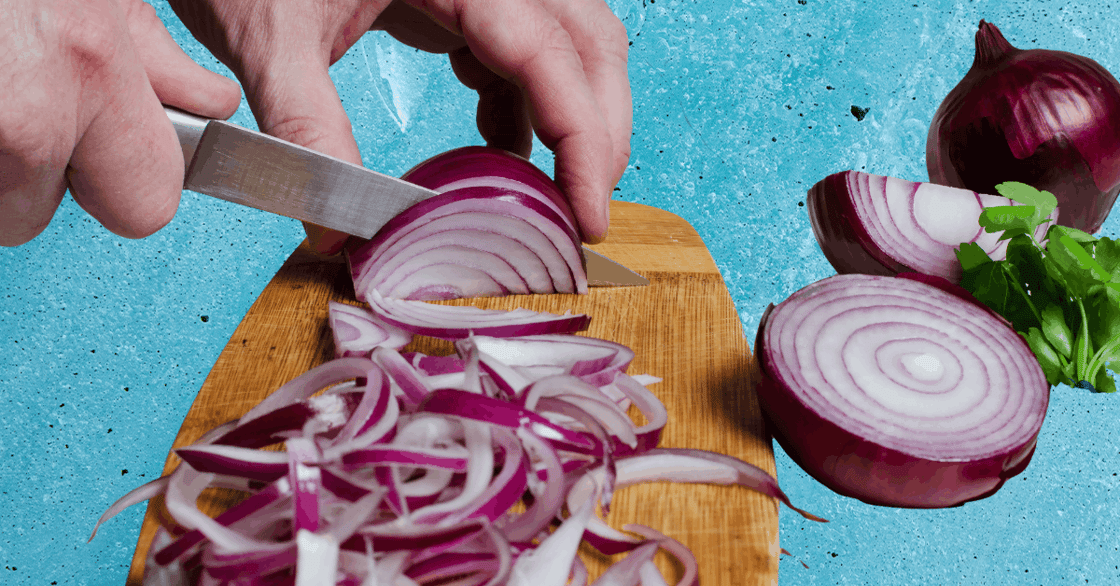 A hand chops a red onion on a cutting board. 