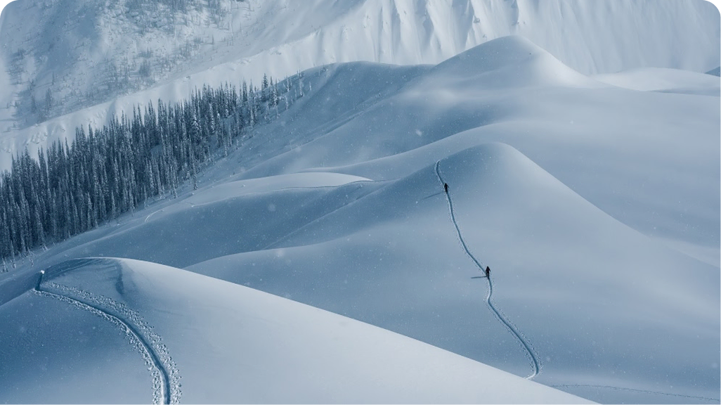 Photo of two backcountry skiers following a skintrack through rolling snow-covered hills.