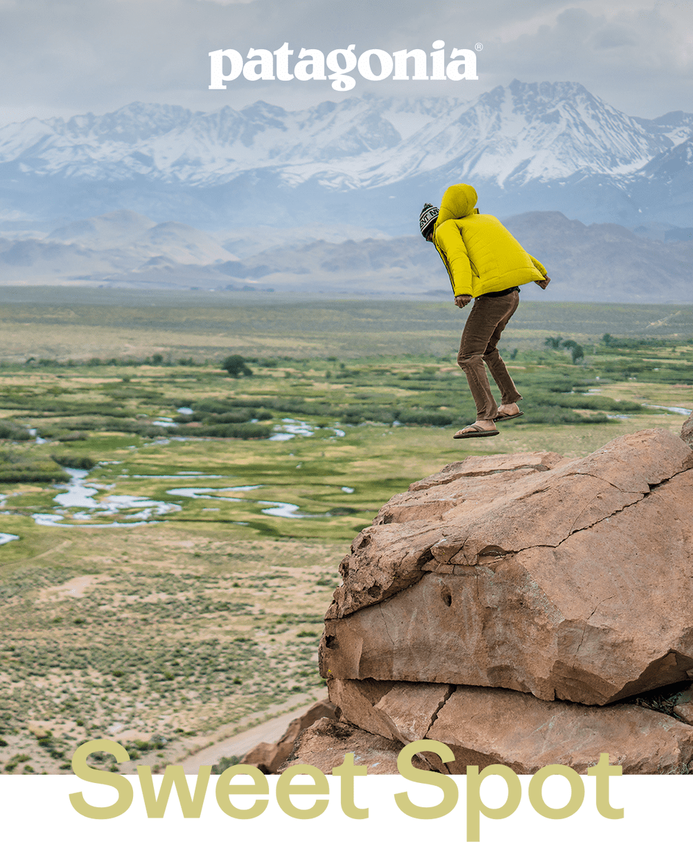 Patagonia. A person jumps on a rock overlooking a river on a windy day.